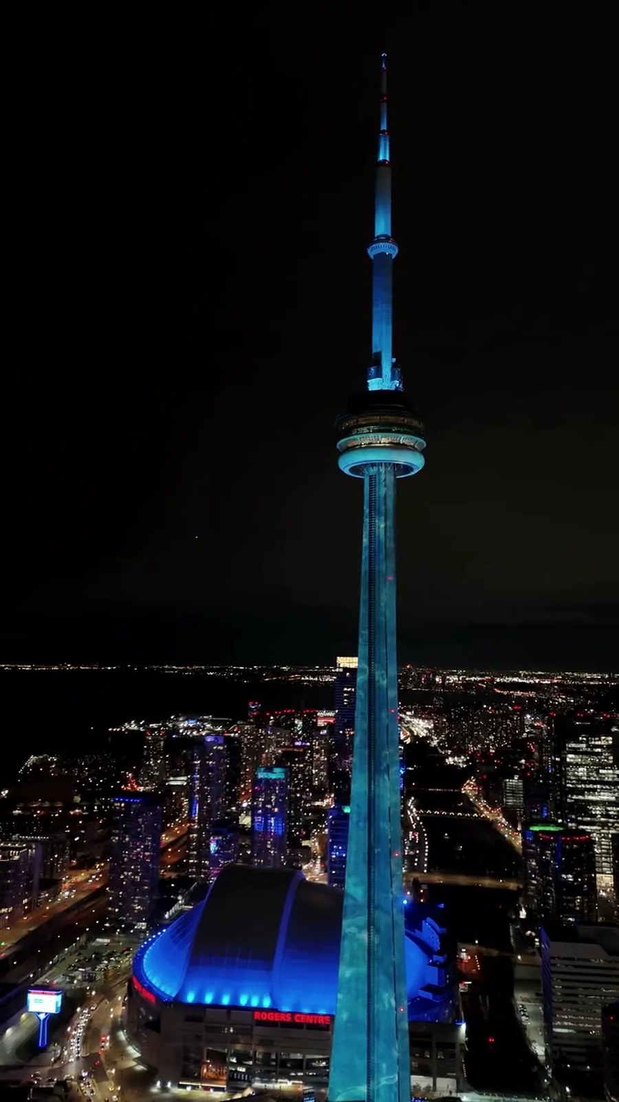 Aerial view of the CN Tower illuminated at night above the Toronto skyline